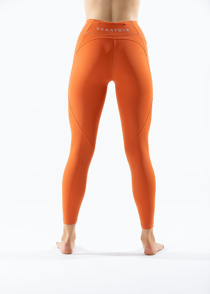 
                  
                    Back side view of sunset orange Venatrix Eva leggings highlighting seamless design, high waistband, and activewear fit.
                  
                
