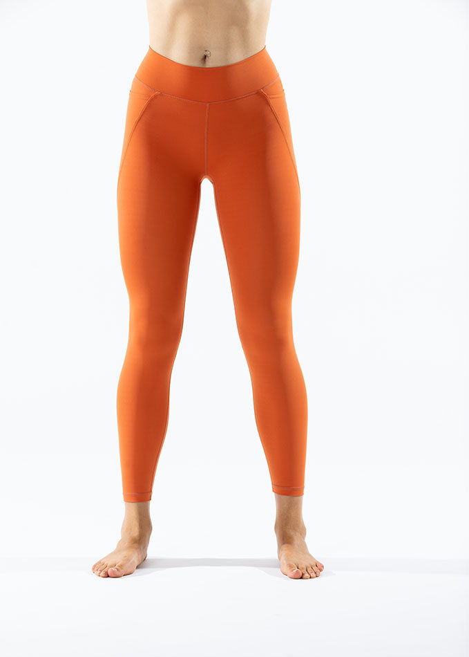 Front view of sunset orange Venatrix Eva leggings with sleek fit, high waistband, and functional side pockets.